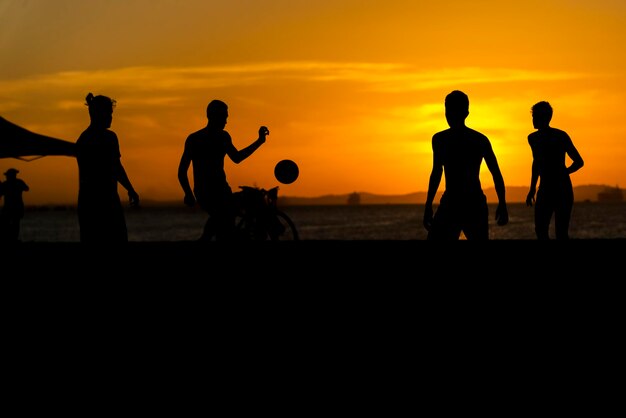 Foto jongeren spelen strandvoetbal bij zonsondergang op het strand van ribeira in salvador bahia, brazilië