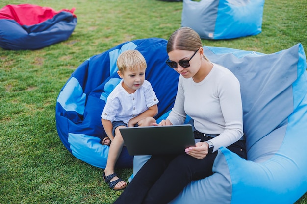 Jongetje met plezier zittend op de zak in de zomer of lente in het park buiten Familievakantie van moeder en zoon in de frisse lucht