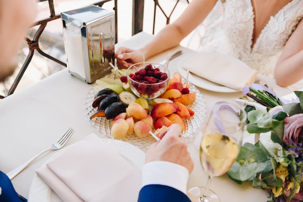 Jonggehuwdebruid en bruidegom die fruit eten en champagne drinken op hun huwelijksdag