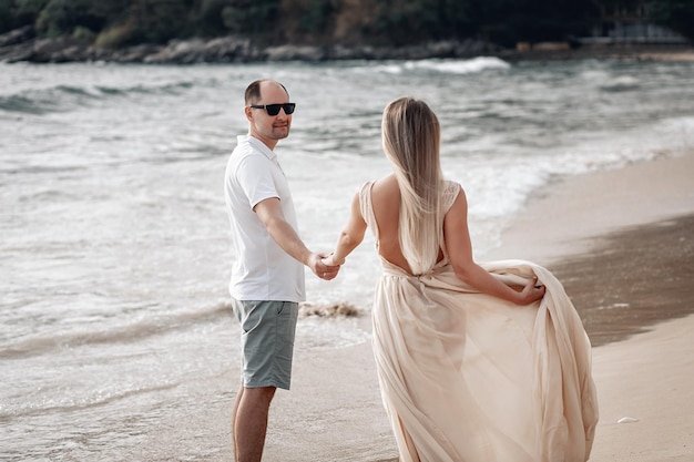 Jonggehuwden gekleed in het wit hand in hand op een exotisch strand zee, zand en liefde; huwelijksreis concept.