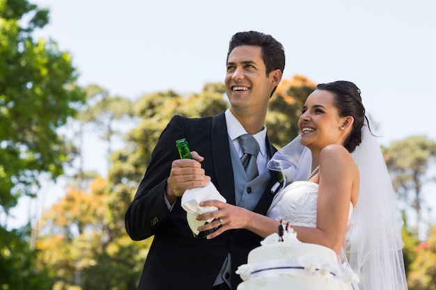 Jonggehuwdepaar met champagnefles bij park