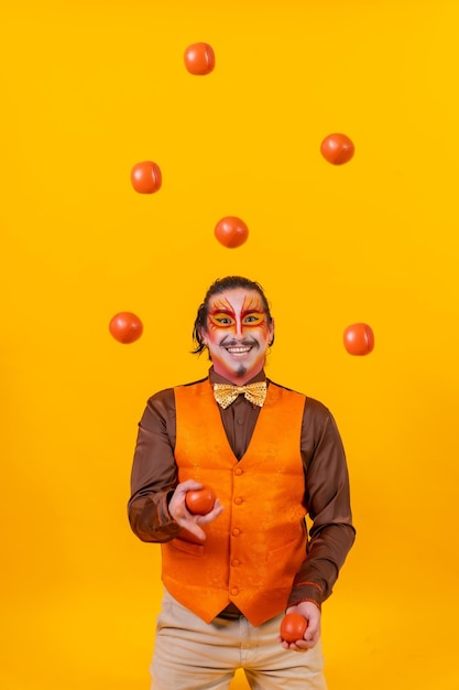 Foto jongleur in een vest en met een geschilderd gezicht jongleerballen op een gele achtergrond