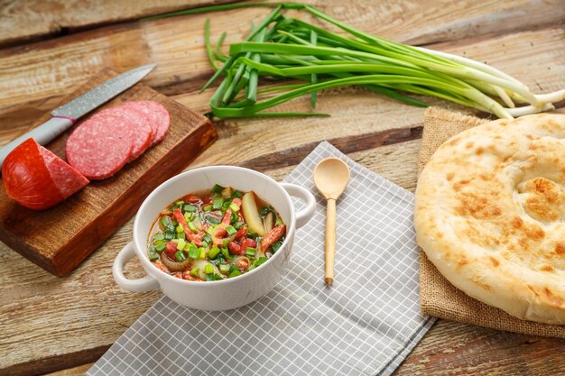 Joodse keukenbonensoep cholit op een grijs servet naast groene uienworst en flatbread