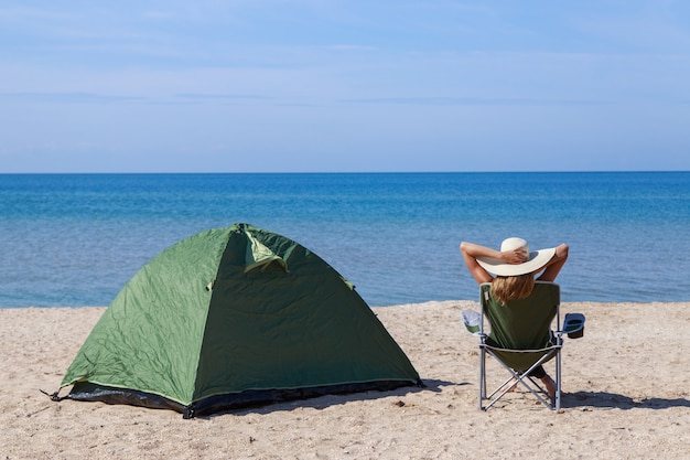 海への旅。ビーチでのキャンプ。水辺での休暇。男性と砂の上に観光用の椅子が付いているテント