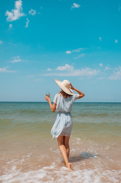 바다로의 여행 드레스와 모자를 쓴 소녀가 해변을 따라 걷고 있다 관광객이 해변을 따라 걷는다...