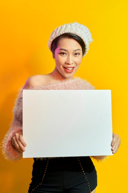 Jouw tekst hier. Mooie jonge opgewonden vrouw met leeg leeg bord. Kleurrijk studioportret met gele achtergrond.