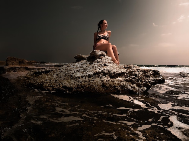 Joven mujer en una roca como una sirena a la luz de la luna junto al mar