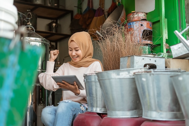 Joy of female seller using tablet with raise hand when surprised in the household appliances store