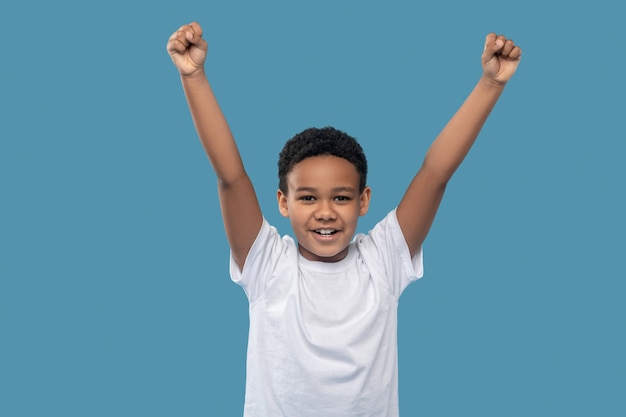 Joy of victory. dark skinned friendly smiling boy in white
tshirt with triumphantly raised fists in studio photo