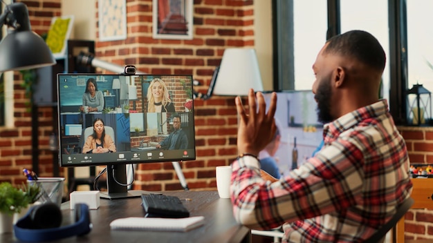 Foto gioioso dipendente afroamericano in una riunione in videoconferenza chiacchierando con un team internazionale multietnico mentre lavora da casa. telelavoratore in videochiamata online con i colleghi