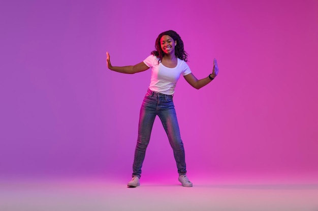 Photo joyful african american female dancing in neon light over purple background