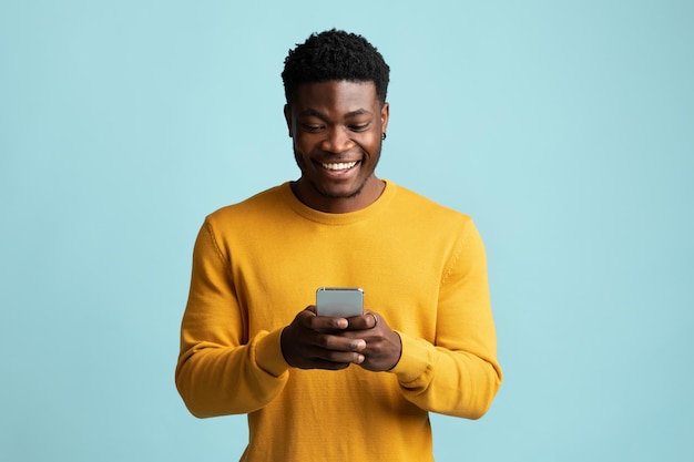 Радостный афроамериканец держит смартфон и улыбается