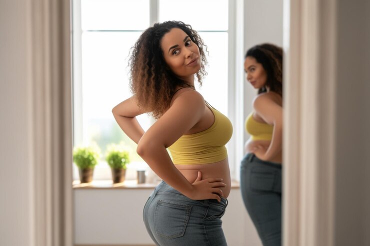 Photo joyful african woman looking at mirror after slimming at home great weight loss joyful african amer