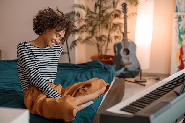 Photo joyful african woman sitting near synthesizer at home