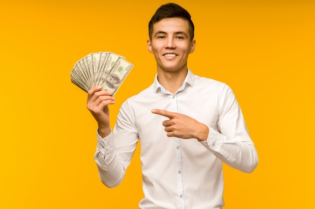 Joyful asian man in a white shirt points a finger at money dollars