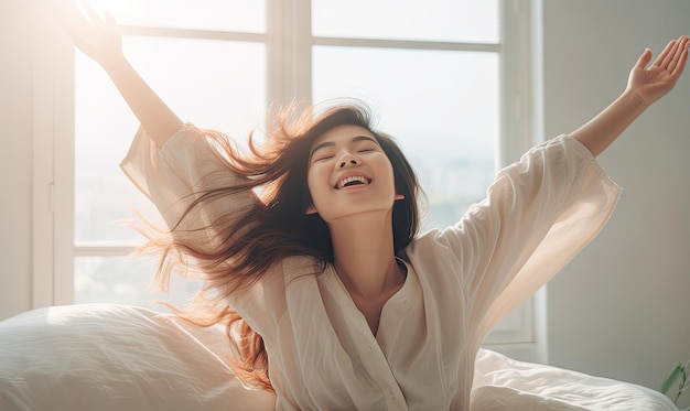 사진 기쁜 아시아 여성은 빛이 비치는 침실에서 스트레칭을 하며 새 날의 평온을 받아들이며 깨어납니다.