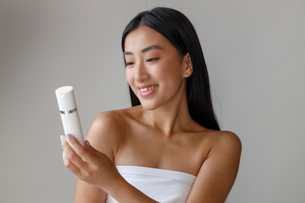 Joyful asian woman holding bottle of cosmetic cream