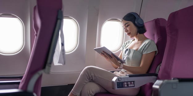 Joyful asian woman sits in the airplane and using tablet while go to travel