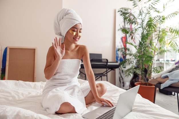 Joyful asian woman using notebook after shower at home