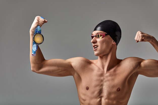 메달을 손에 들고 즐거운 수영 선수는 긍정적인 감정, 승리의 기쁨, 성공의 개념, 결코 포기하지 않고 성공을 달성할 것입니다.