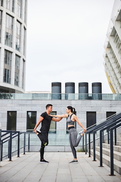 Joyful athletyic man and woman are stretching legs during workout on stairs to stadium in city centre