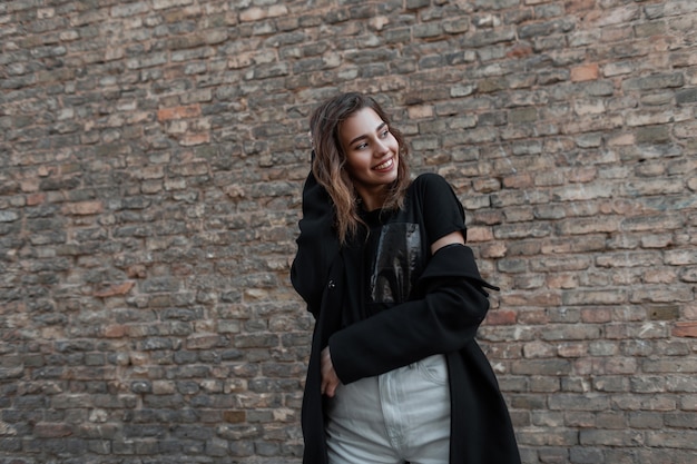 Joyful attractive young woman with a cute smile in a stylish coat in a black outwear