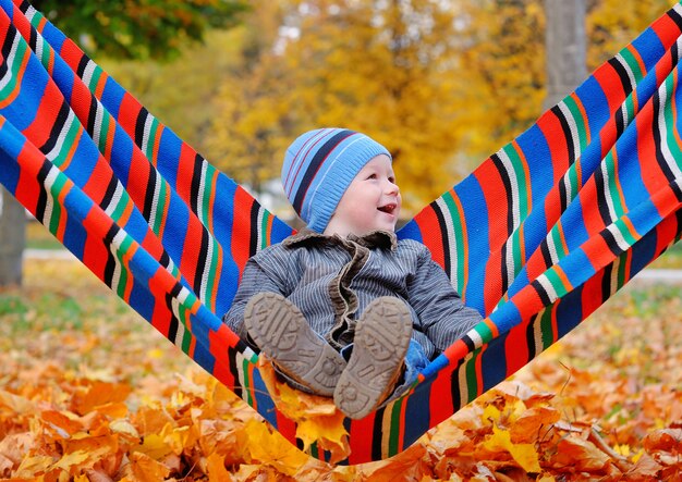 Joyful baby boy in autumn park on a hammock