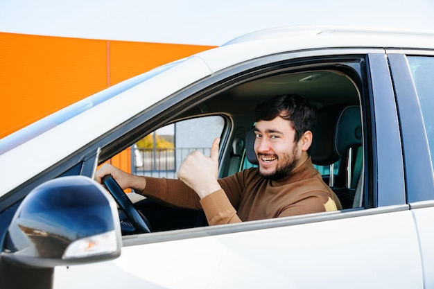 Joyful bearded caucasian man showing thumb up and looking at the camera is in the car driver smiling