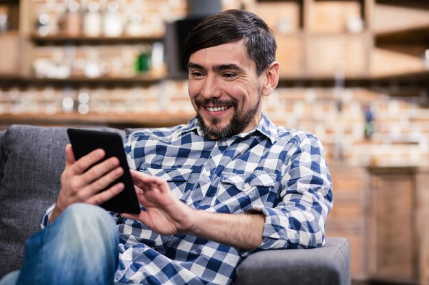 Joyful bearded man resting at home while using his tablet