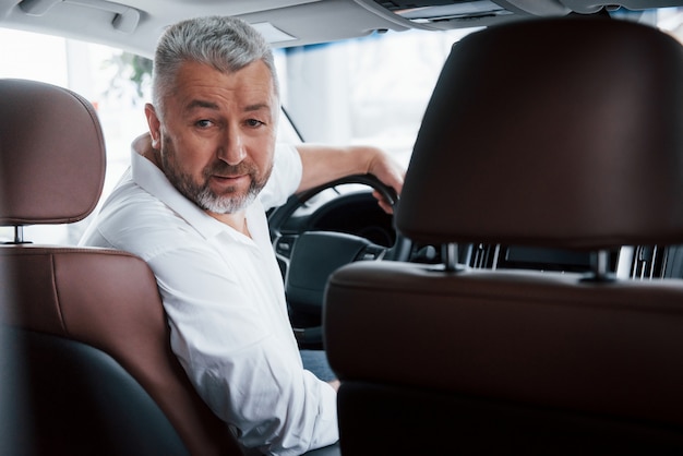 Joyful bearded man in white shirt while sitting in the modern car