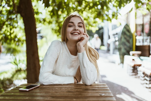 Joyful beautiful blonde smiles amiably sitting at a table of a street cafe