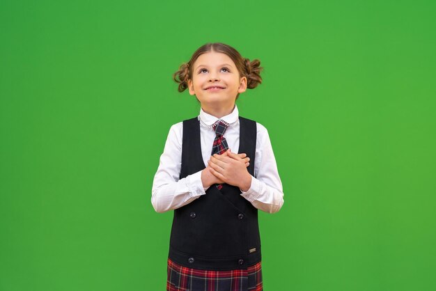 A joyful and beautiful school girl looks up with a smile a schoolgirl on an isolated green background