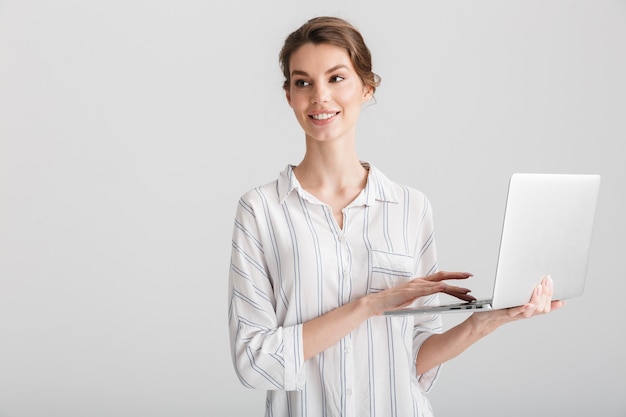 joyful beautiful woman smiling and typing on laptop isolated over white background