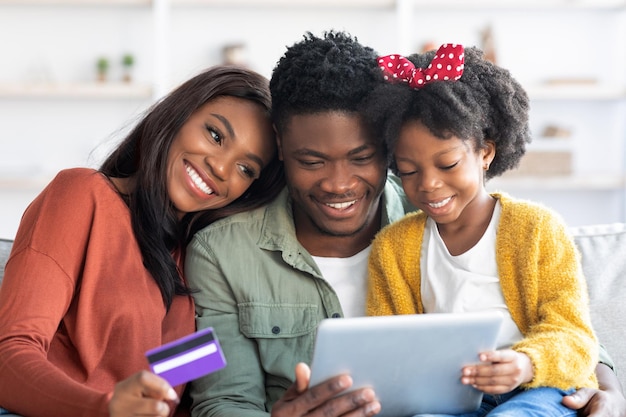 Joyful black family using digital tablet and credit card for online shopping