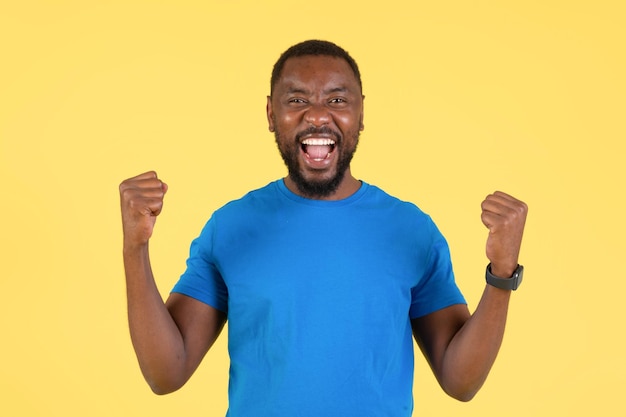 Радостный черный парень трясет кулаками от радости на желтом фоне