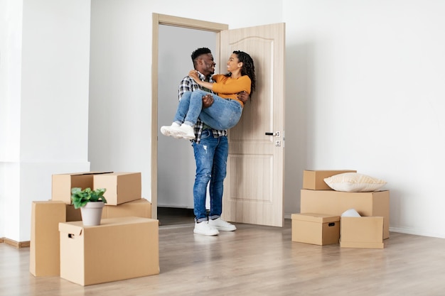 Photo joyful black husband carrying wife entering house after relocation indoor