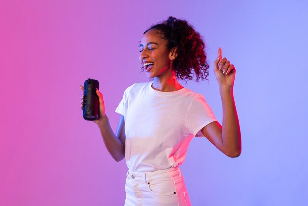 Joyful black lady dancing with portable speaker on gradient background