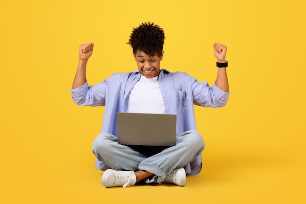 Photo joyful black male student with laptop celebrating success