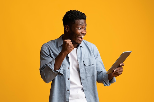 Joyful black man looking at digital tablet screen and gesturing