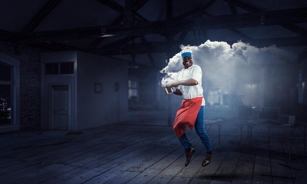 Joyful black man wearing an apron and cooking in action. Mixed media