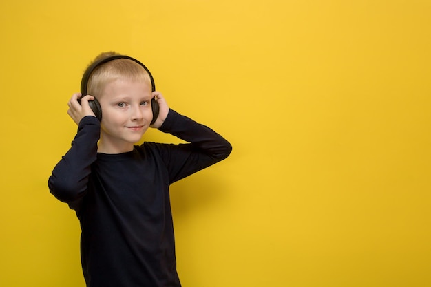 Joyful boy listens to something in headphones on a yellow background with copy space