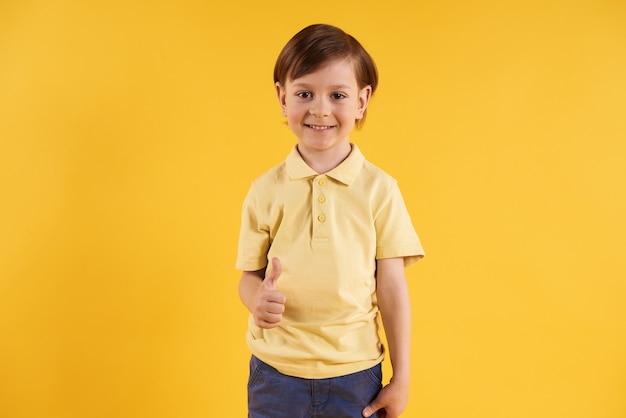 Joyful boy in t-shirt showing thumbs up.