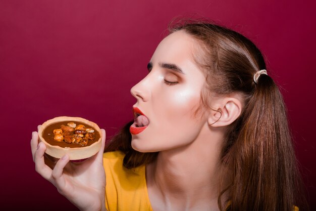 Joyful brunette girl with red lips having fun with tart cake. Studio shot