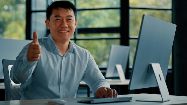 Joyful businessman asian mature chinese japanese man office manager work on computer make thumb up