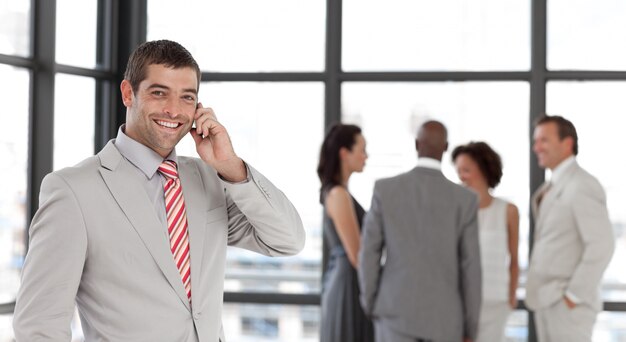 Joyful businessman holding a phone at workplace with his colleagues 