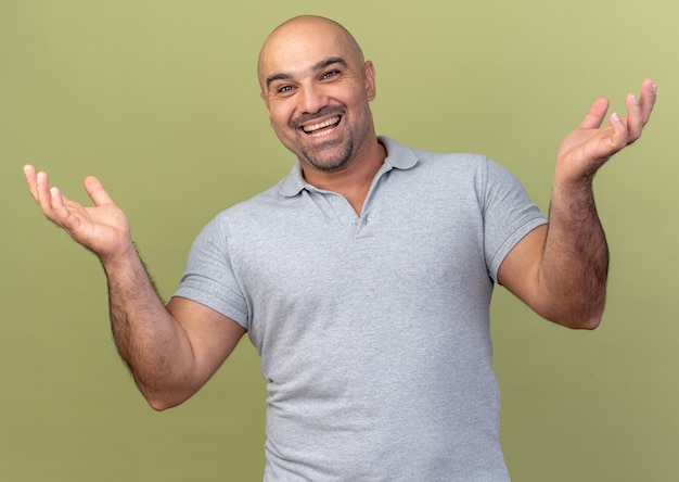 Joyful casual middle-aged man  showing empty hands isolated on olive green wall