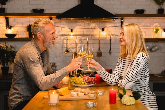 Joyful caucasian mature couple celebrating anniversary or StValentines day during romantic dinner in the kitchen