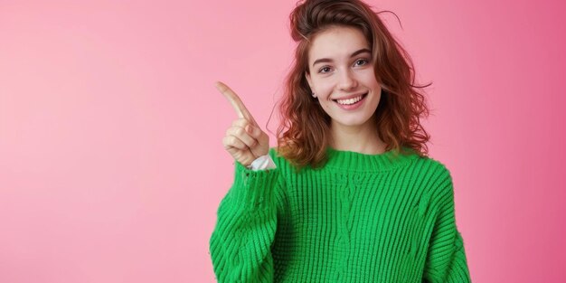 Joyful Caucasian Woman Pointing Upwards in Bright Green Sweater Pink Background