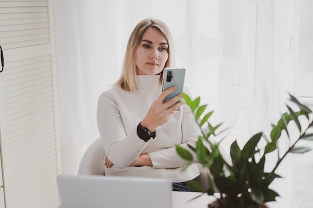 Joyful charming woman using laptop and mobile phone smiling while sitting at the workplace