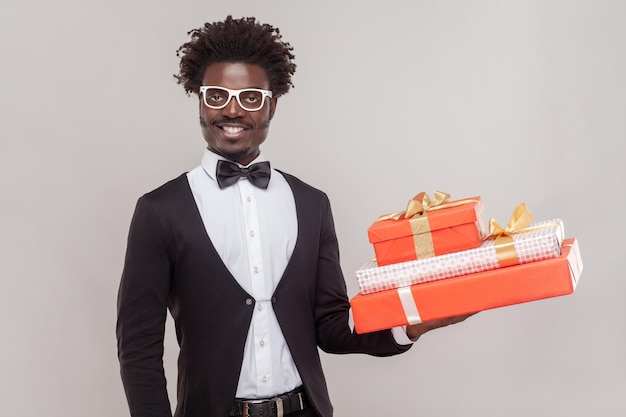 Joyful cheerful man in glasses standing holding three present boxes being in festive mood